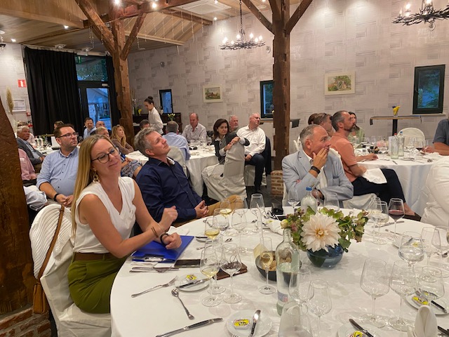 Leden luisteren aan tafel naar de keynote